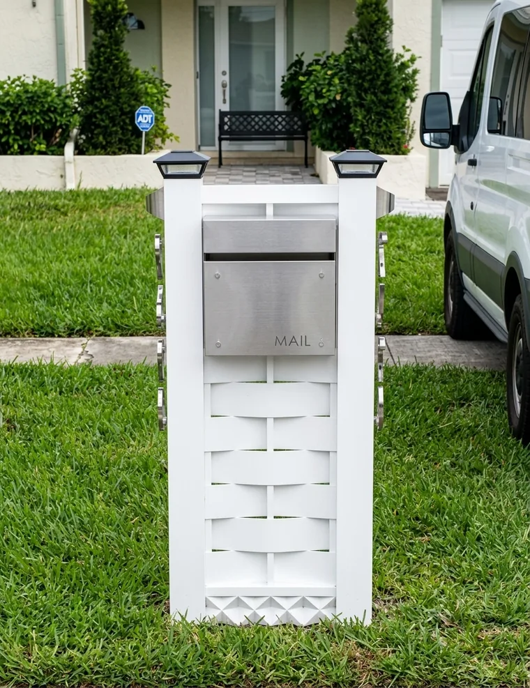 Pedestal blanco con lamas y buzón de acero inoxidable al frente de una casa