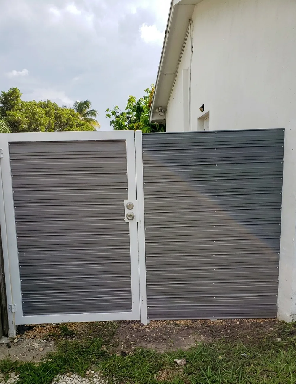 Puerta de aluminio de lama fina con marco blanco en el acceso a un patio