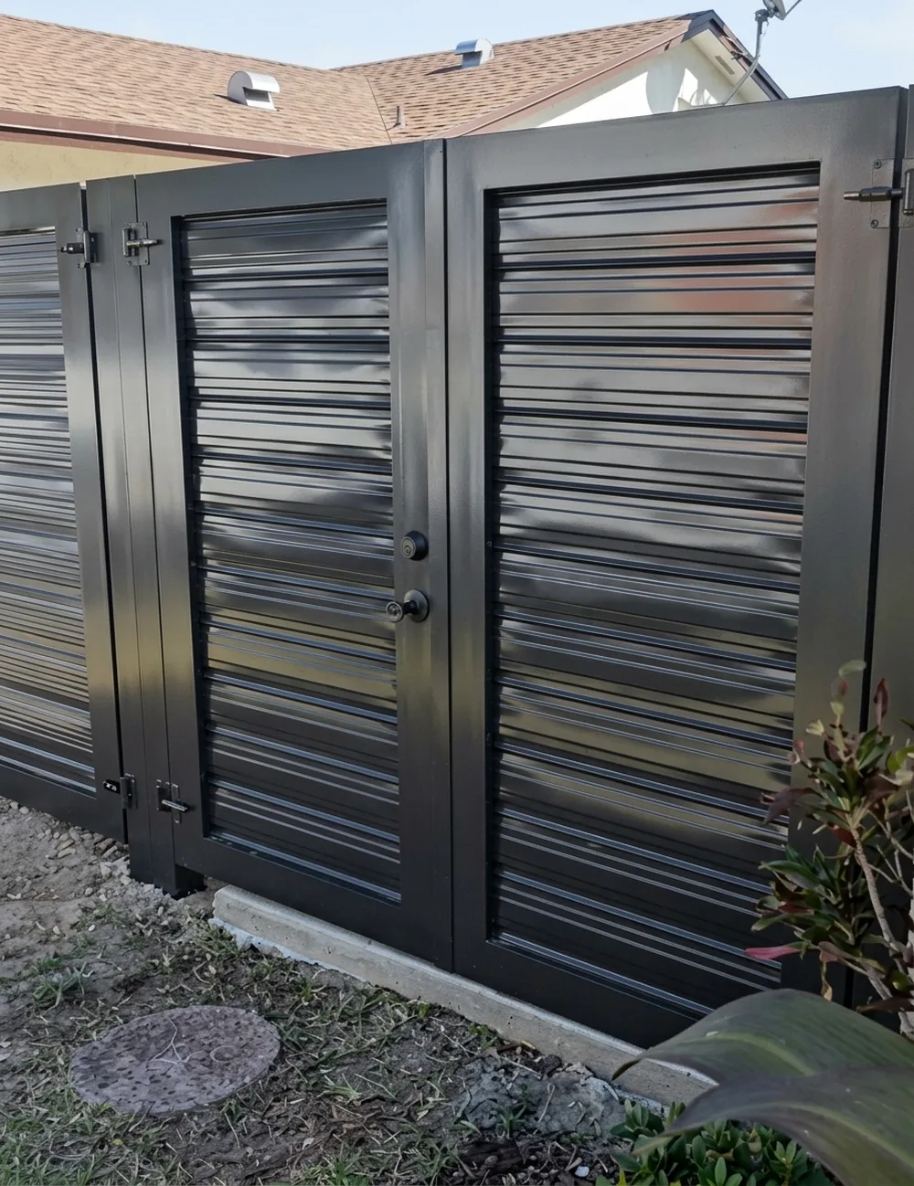 Puerta doble oscura de lama vertical instalada al costado de una vivienda